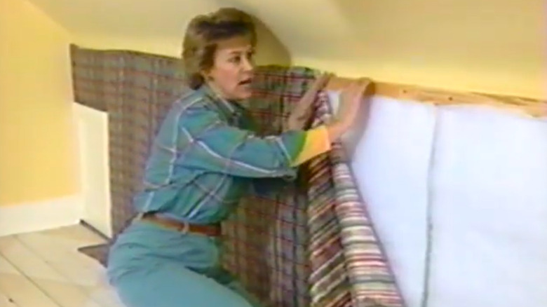 A woman crouching while installing fabric on a wall.