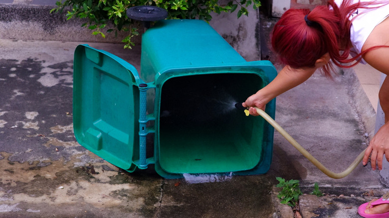 Woman hosing out a garbage can