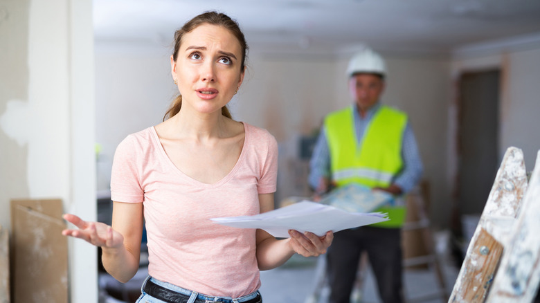 A portrait of confused apartment owner holding document with contractors in the room