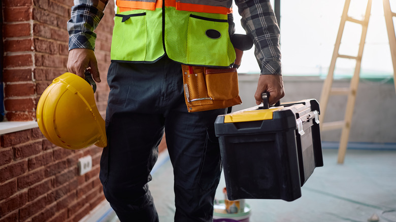 A construction worker holding a hard hat and a toolbox