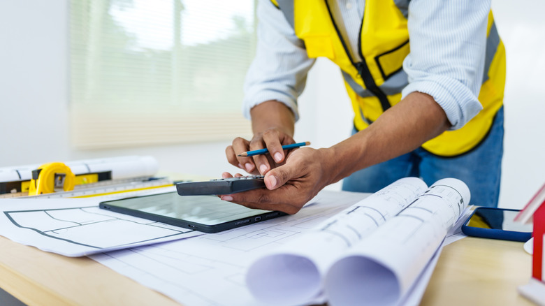 A contractor bent over a desk examining construction plans, permits, and other important paperwork