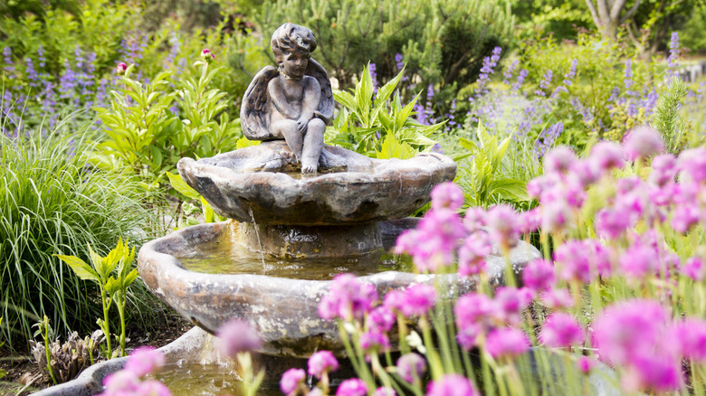 A water feature of an angel in a flower garden.