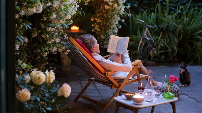 A woman lounging on her patio reading a book next to candles.