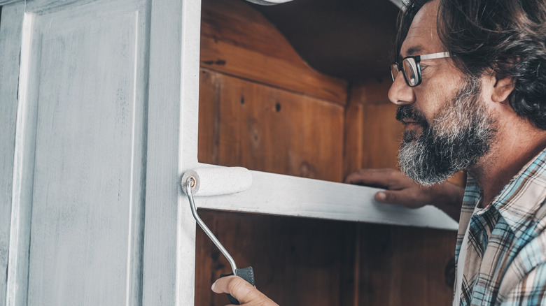 Close up of mature man painting and restoring an old antique wooden cabinet