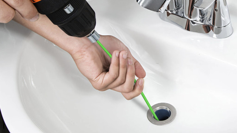 A person using the drill-mounted auger from TubShroom's Universal Drain Protector and Hair Catcher Bundle