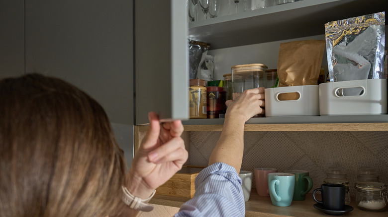 A person reaching for a jar in a well-organized kitchen cabinet