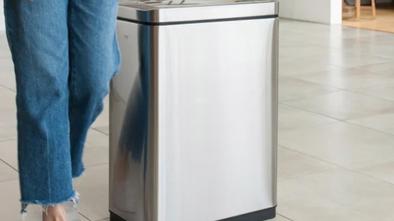 A female standing beside a stainless steel trash can