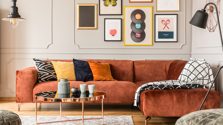 A living room features a burnt-orange velvet sofa, eclectic gallery wall, and a rose gold coffee table