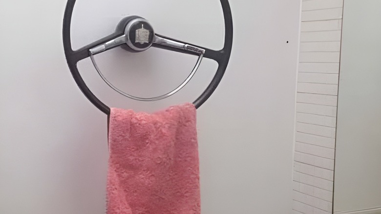 A pink towel hanging on a steering wheel in a bathroom.