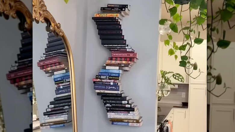 Curvy bookshelf hanging on wall with gold mirror and vining plants