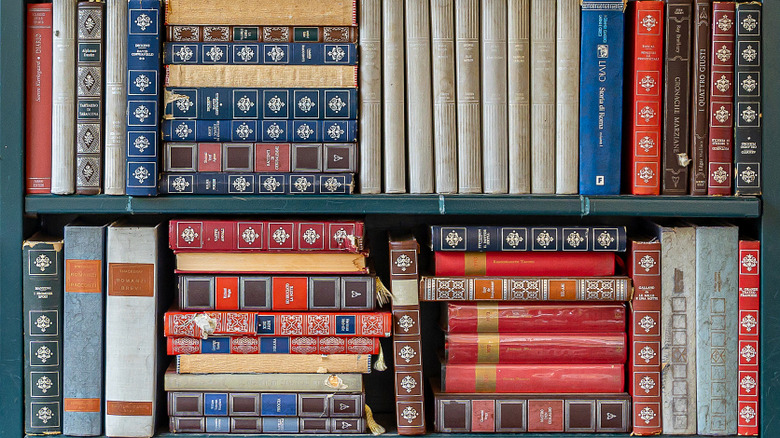 Colorful stacks of books placed vertically and horizontally on green wall shelf