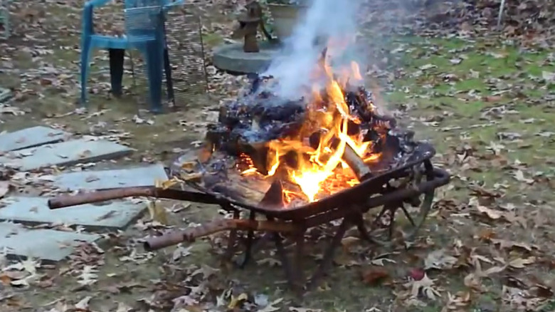 A wheelbarrow being used as a fire pit with burning logs