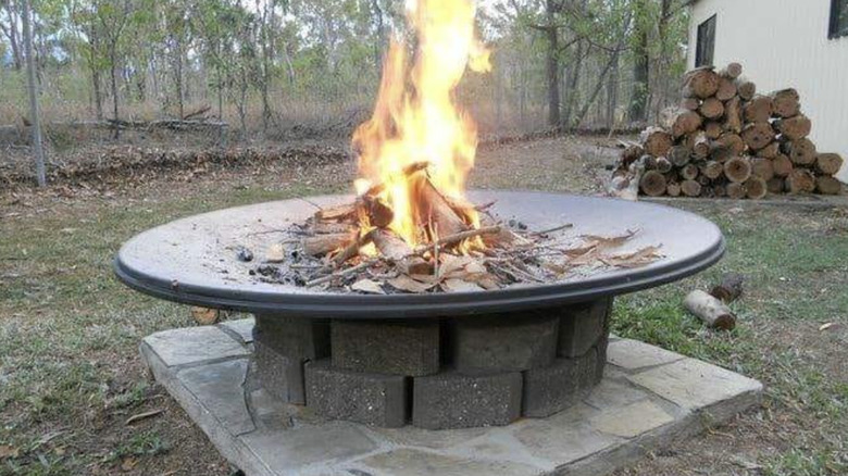 Satellite dish fire pit in a yard with burning wood