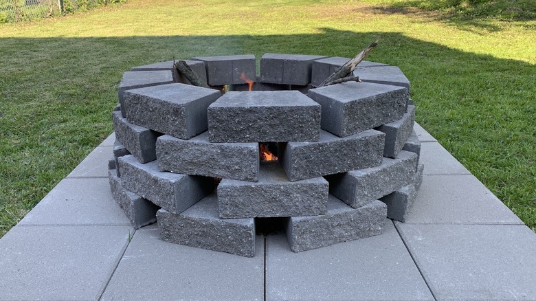 A wall block fire pit on large pavers in a yard