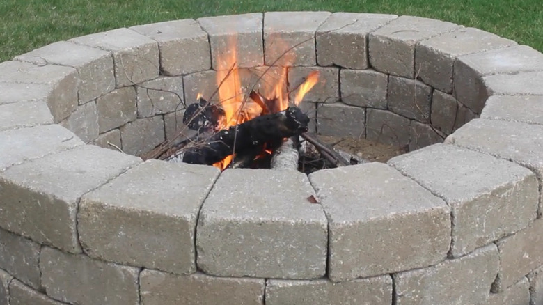 A fire pit made of stone pavers with burning logs