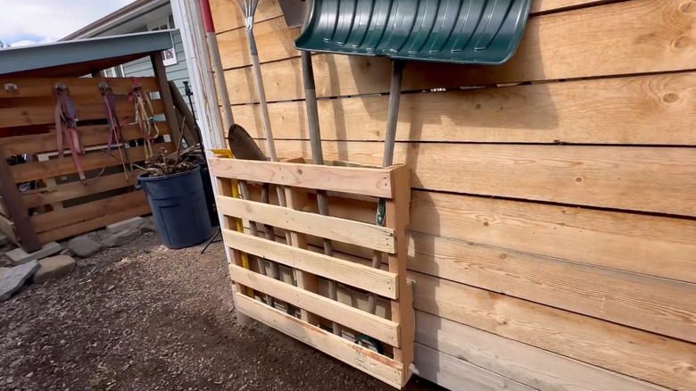 An old pallet turned into a garden tool holder on the side of a building