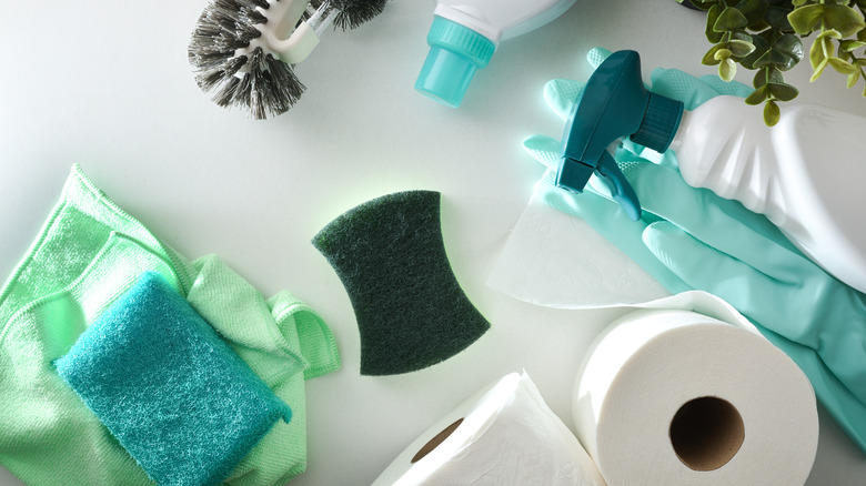 green scrubbers, toilet paper, and a spray bottle laying on a white surface.
