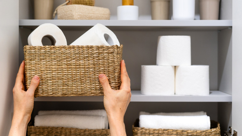 A woman placing a wicker basket filled with toilet paper on a shelf