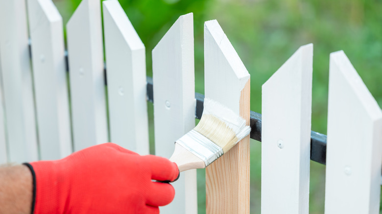 A painter painting a white picket fence