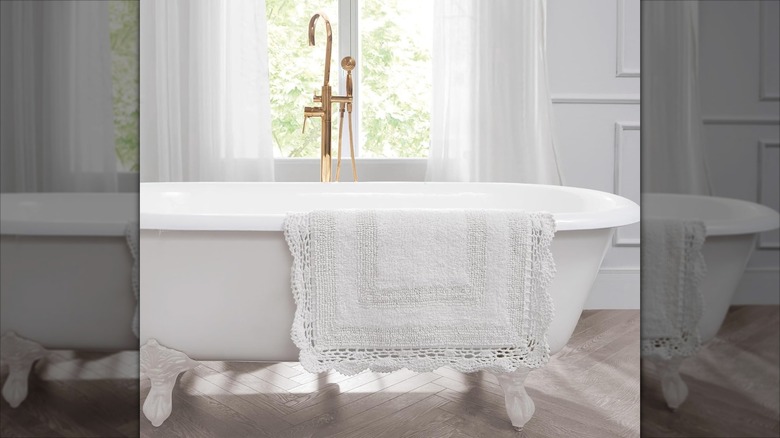 A white crocheted bath mat is draped over a standing tub