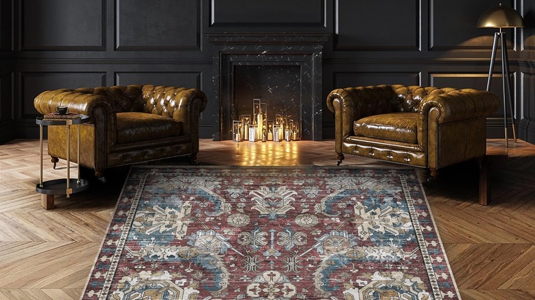 Two tufted leather armchairs flank a patterned rug in front of a candlelit fireplace