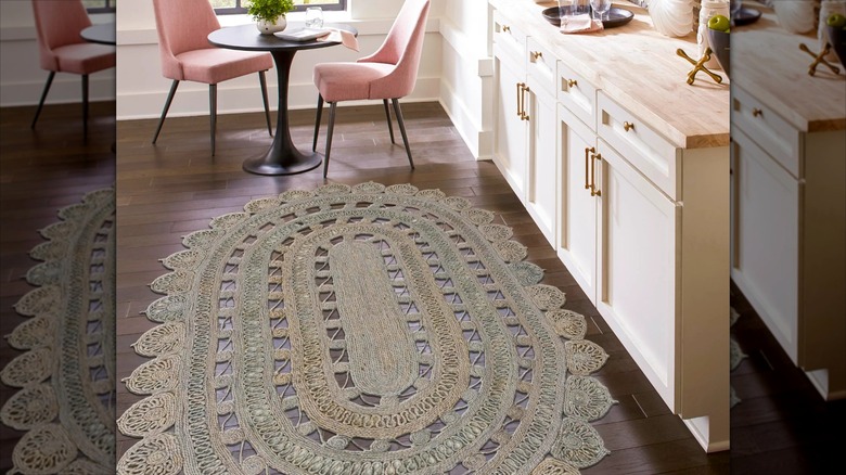 A hand-braided natural jute floor rug lays in front of kitchen cabinets and two pink velvet side chairs
