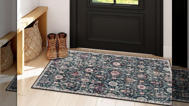 A pair of boots sit on a thin multicolored entryway rug in front of a black exterior door