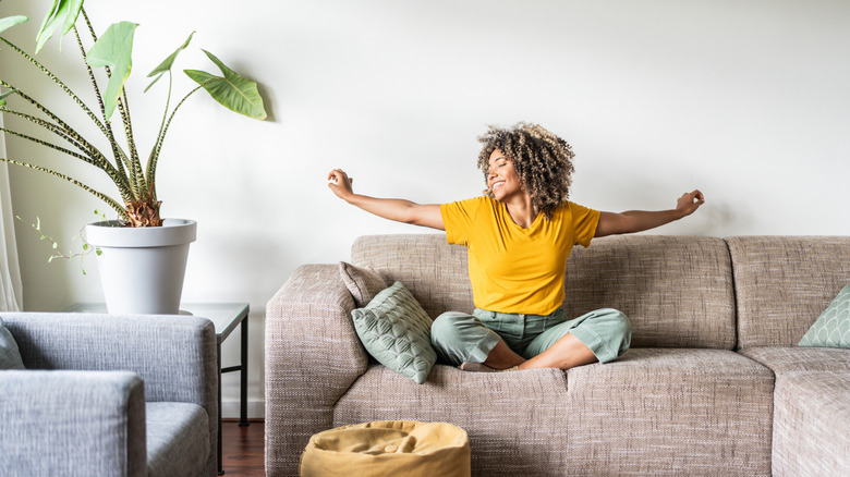 A person happily relaxing and stretching on a living room sofa