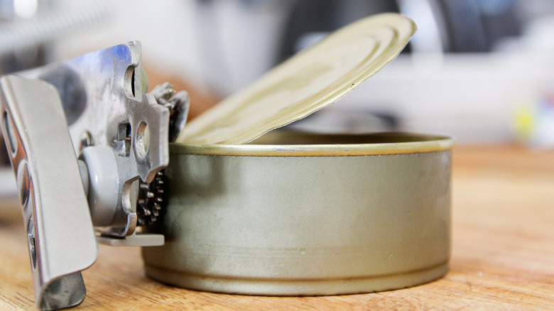 A manual opener takes the lid off an unlabeled tuna can.