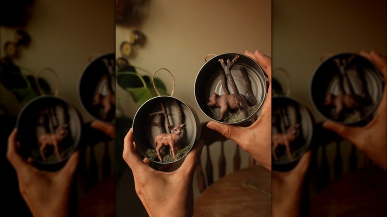 Tuna cans hung sideways hold a woodland scene.