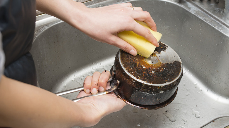 A person washing the base of a dirty pan