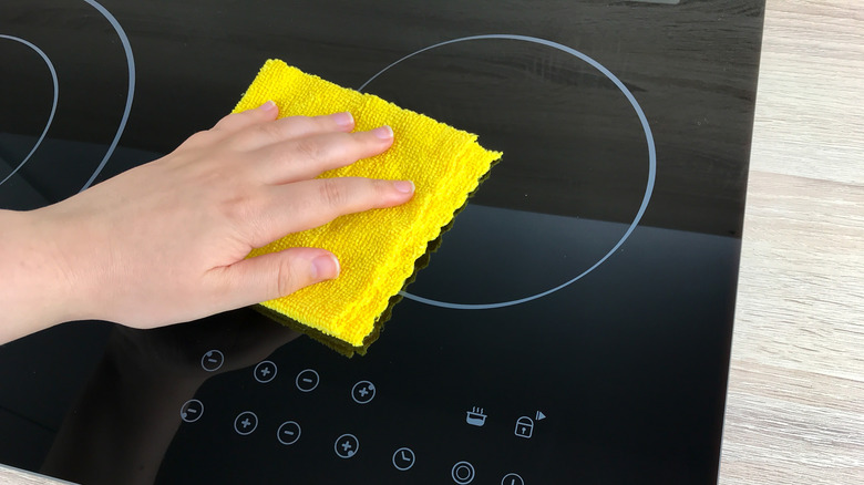 Close-up of a person wiping a glass stove with a dry cloth