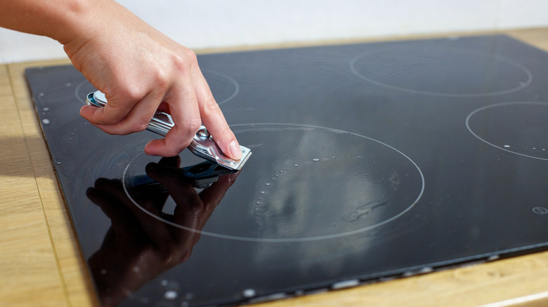 A person scraping the surface of a glass stove with a razor scraper