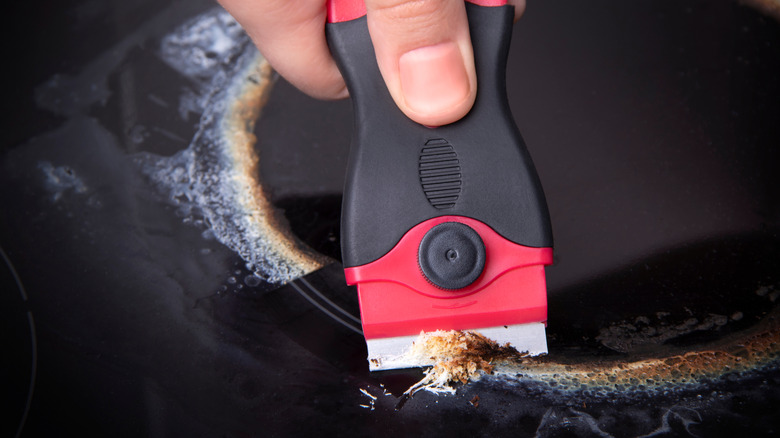 Close-up of a person scraping a heavily-soiled glass stove stop