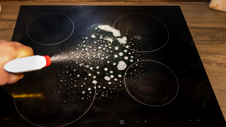 A person spraying a glass stove top to soak