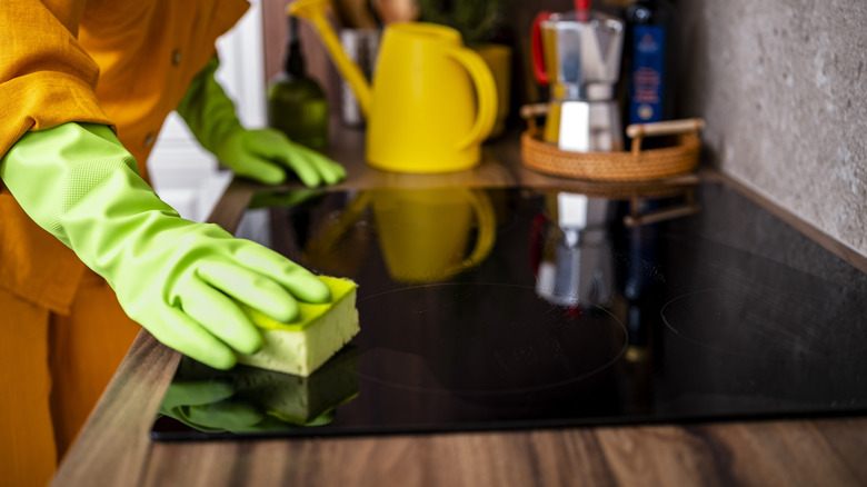 A person in green gloves gently wiping the surface of their stove