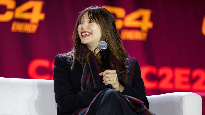 Elizabeth Olsen holding a microphone and sitting on a stage during a panel