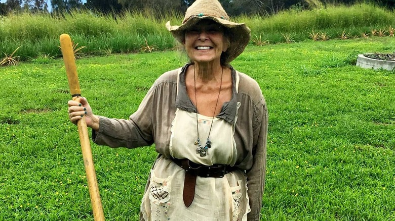 Roseanne Barr standing on her farm and holding a gardening tool