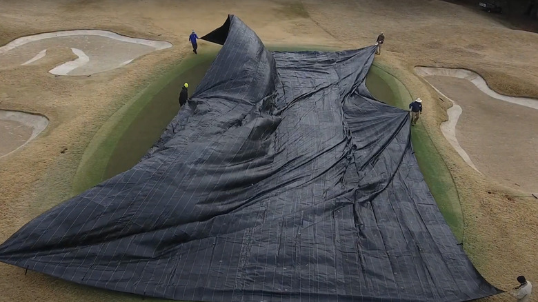 workers installing a tarp on golf green
