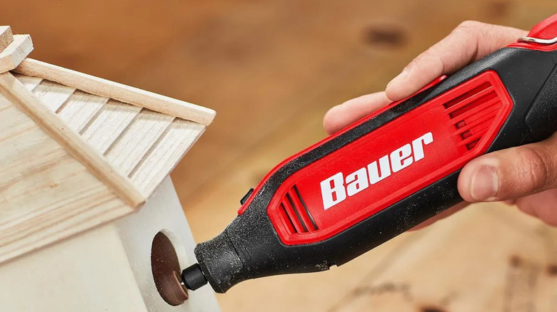 A person using Bauer's 1.6 Amp Variable Speed Rotary Tool Kit to sand a wooden birdhouse