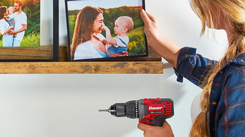 A woman holding Bauer's 20V Brushless Cordless, ½-inch Drill/Driver while arranging photographs on a shelf