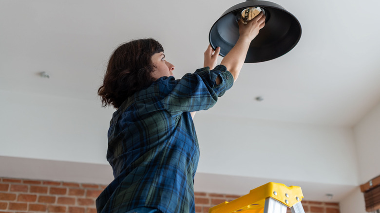 A woman on a step ladder changing a lightbulb