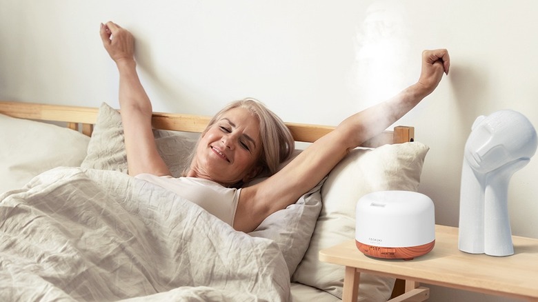 An essential oil diffuser on a table beside a woman waking up