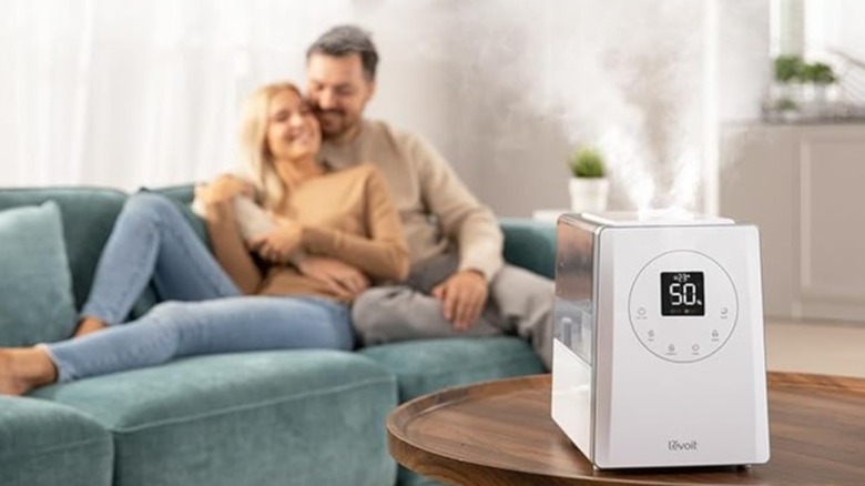 A white humidifier misting in a living room where a couple is sitting on the sofa