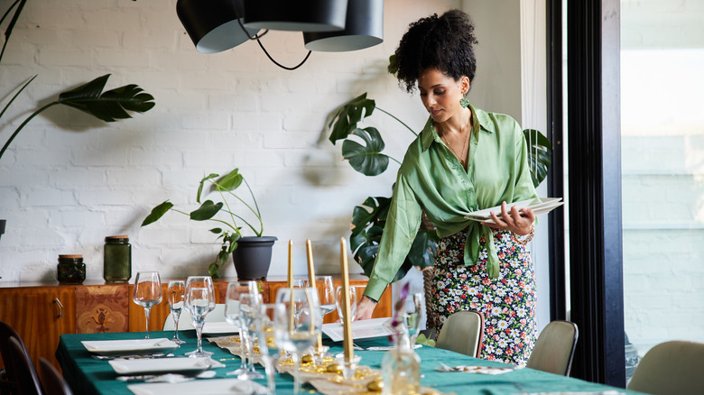 A woman carefully sets plates at a dining room table
