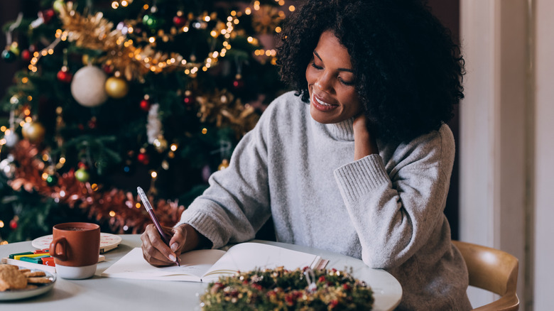 A woman at a table writing in a notebook with a Christmas tree in background