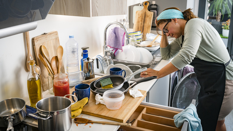 Woman bent over a disorganized kitchen countertop and sink area