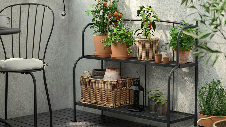 IKEA's LÄCKÖ two-tier shelving unit on a balcony, laden with plants, pots, and other outdoor equipment