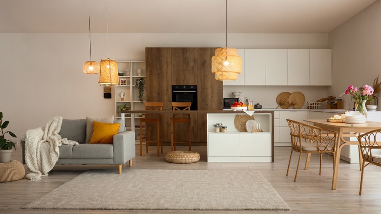 Interior of modern open plan kitchen with dining table, island, gray sofa, and glowing lamps