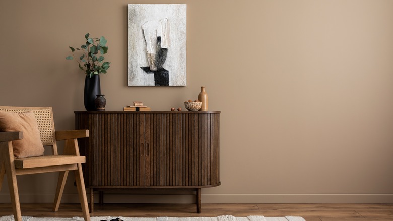 Creative composition of living room interior with mock up poster frame, copy space, wooden sideboard, vase with branch, rattan armchair, beige rug and personal accessories.